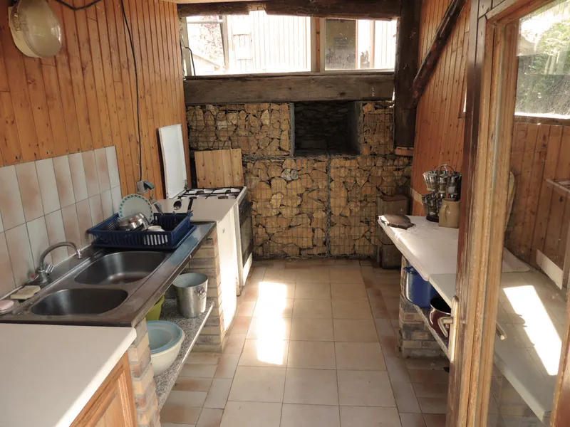 Cuisine rustique avec évier double, plaques de cuisson et four, murs en pierre et poutres apparentes