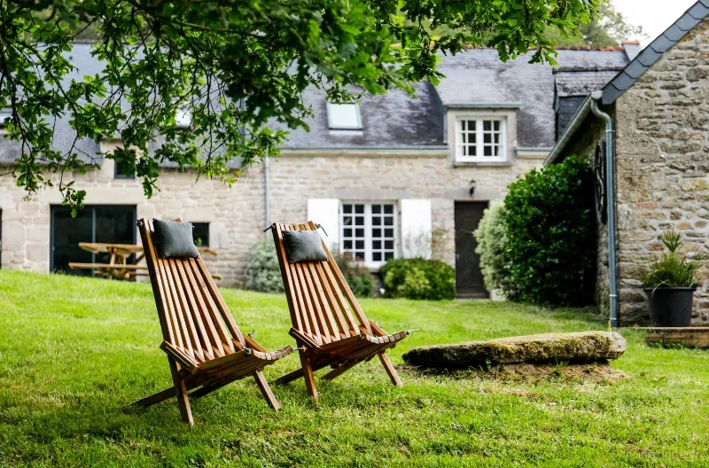 Deux chaises longues en bois dans le jardin face à la façade en granit des longères