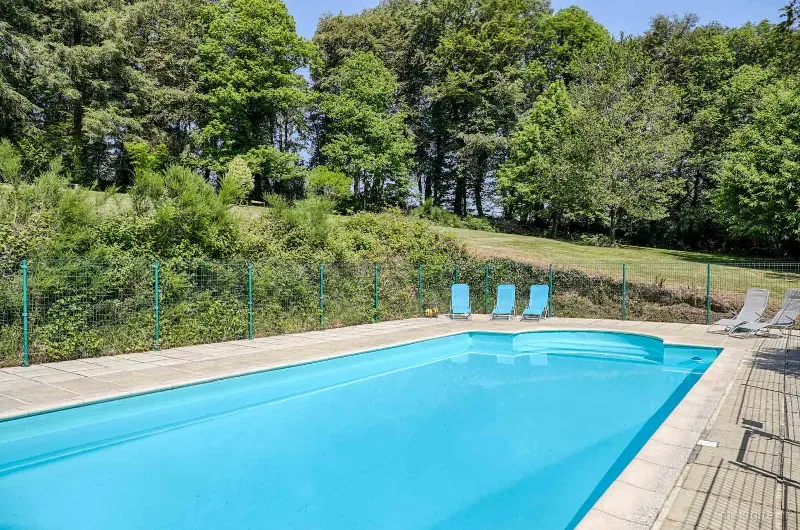 Piscine extérieure chauffée et sécurisée avec transats bleus, bordée d'arbres et de verdure