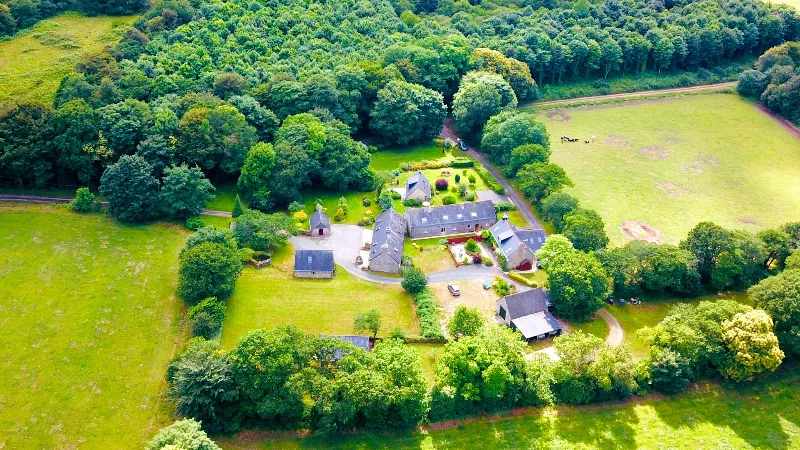 Vue aérienne du hameau de Kernolo avec ses six bâtiments en granit entourés de champs verts et de forêt bretonne