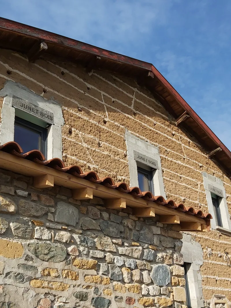 Façade en pierres dorées du Domaine de Solémy sous un ciel bleu avec vignoble en arrière-plan