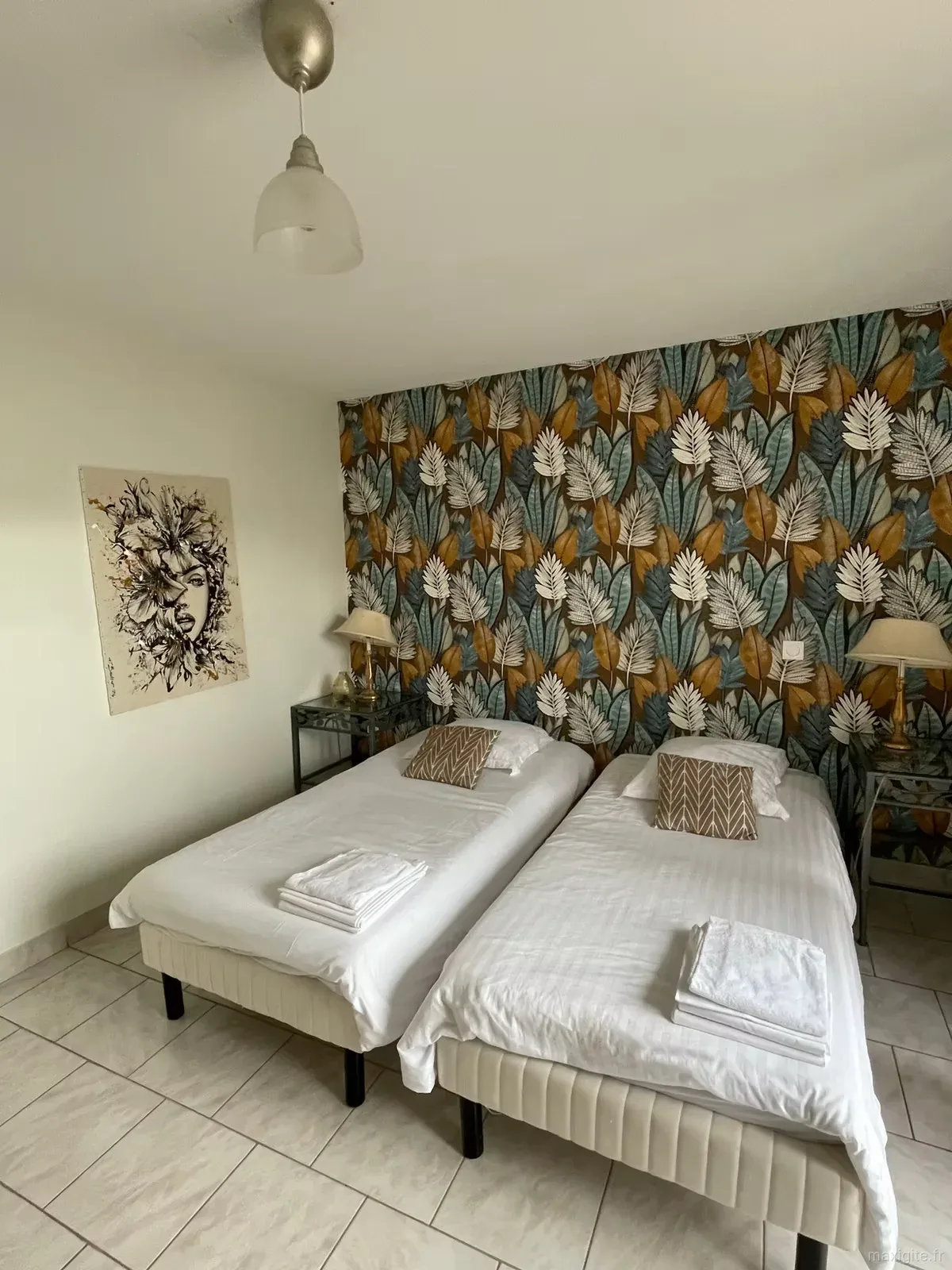 Chambre jumelle avec papier peint à motifs de feuilles bleues et dorées, lits habillés de blanc et coussins marron