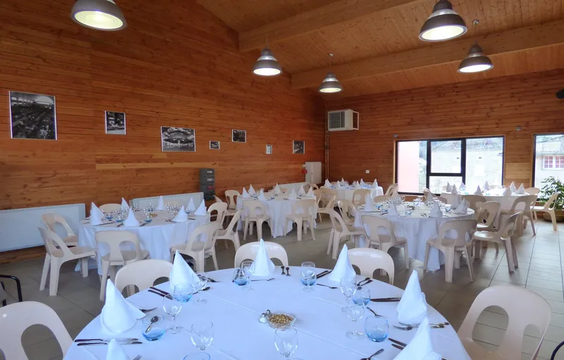 Grande salle de réception avec tables dressées en nappes blanches, murs et plafond en bois