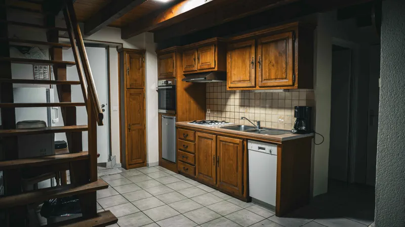 Cuisine équipée en bois avec plaque de cuisson, four encastré et lave-vaisselle, escalier visible à gauche
