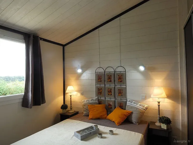 Chambre mansardée avec tête de lit en fer forgé à cadres photo et coussins orange sur couvre-lit blanc