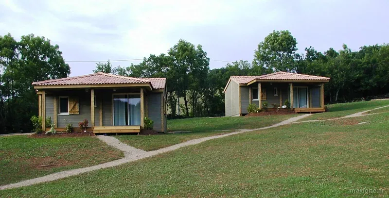Deux chalets en bois à toit de tuiles orangées posés sur une pelouse verdoyante, chemin de gravier menant à l'entrée