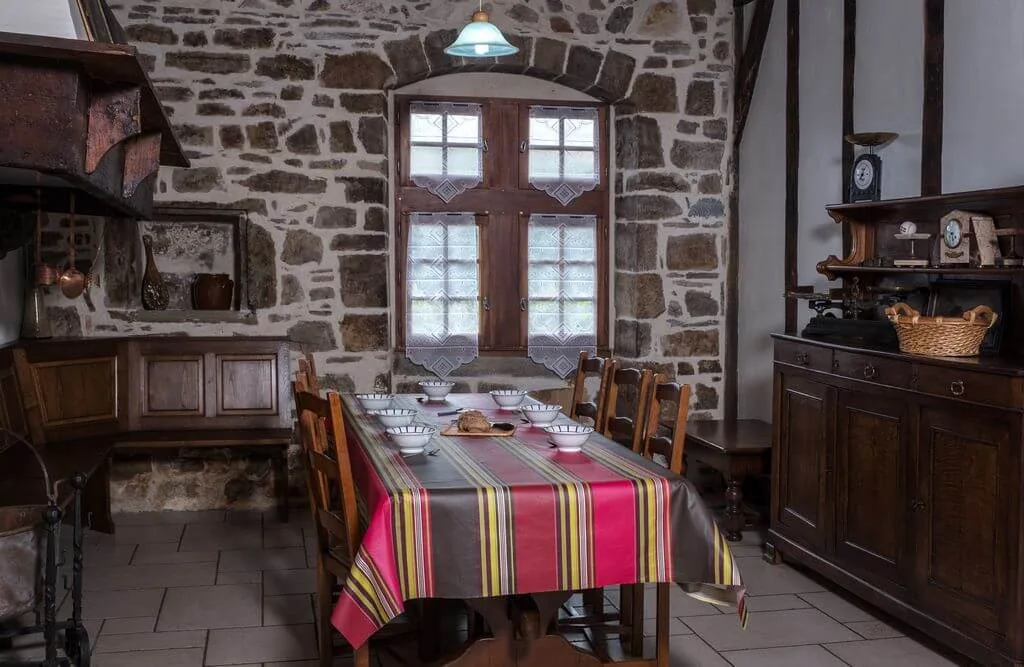 Coin repas voûté en pierre avec fenêtre à rideaux brodés, buffet ancien et balance de cuisine ancienne