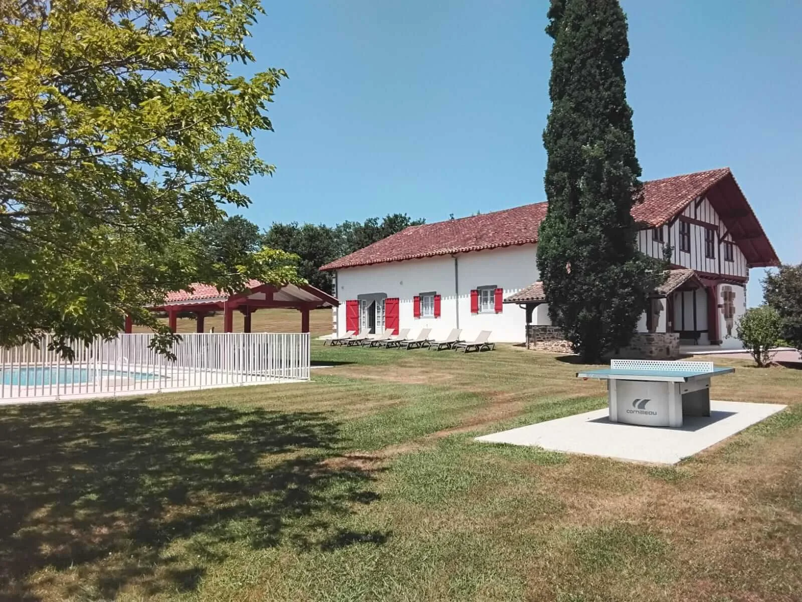 Gîte de groupe Domaine Basque Eyhartzea à La Bastide-Clairence — Ferme basque blanche à colombages rouges et volets rouges, piscine clôturée et table de ping-pong sur la pelouse, capacité 18 personnes