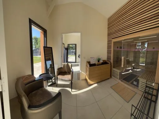 Espace détente avec fauteuils en cuir et sauna à cabine de bois clair visible à travers une paroi vitrée