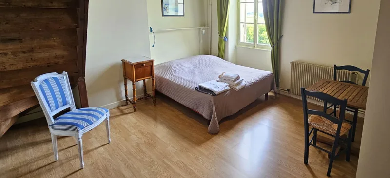 Chambre claire avec lit double, chaise rayée bleue et parquet blond