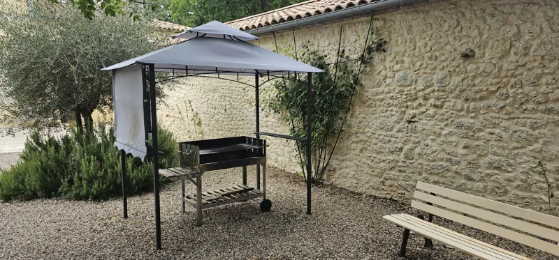 Barbecue sous pergola métallique dans cour en graviers et mur en pierre