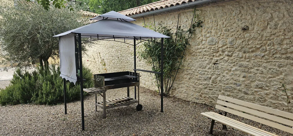 Gîte de groupe Domaine aux Trois Fontaines à Eynesse — Barbecue sous pergola métallique dans cour en graviers et mur en pierre, capacité 30 personnes