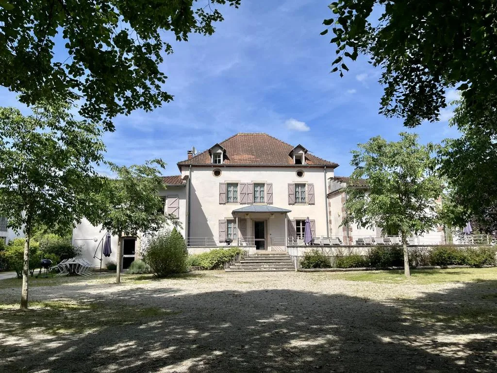 Gîte de groupe Gîtes des Thermes à Féneyrols — Façade principale du bâtiment Le Goutal avec ses volets bleus et son jardin, capacité 18 personnes